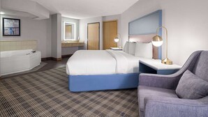 A modern hotel room with a large bed, a sitting area, a bathroom with a bathtub, and a large mirror. - AmericInn by Wyndham Shakopee Near Canterbury Park (Shakopee)