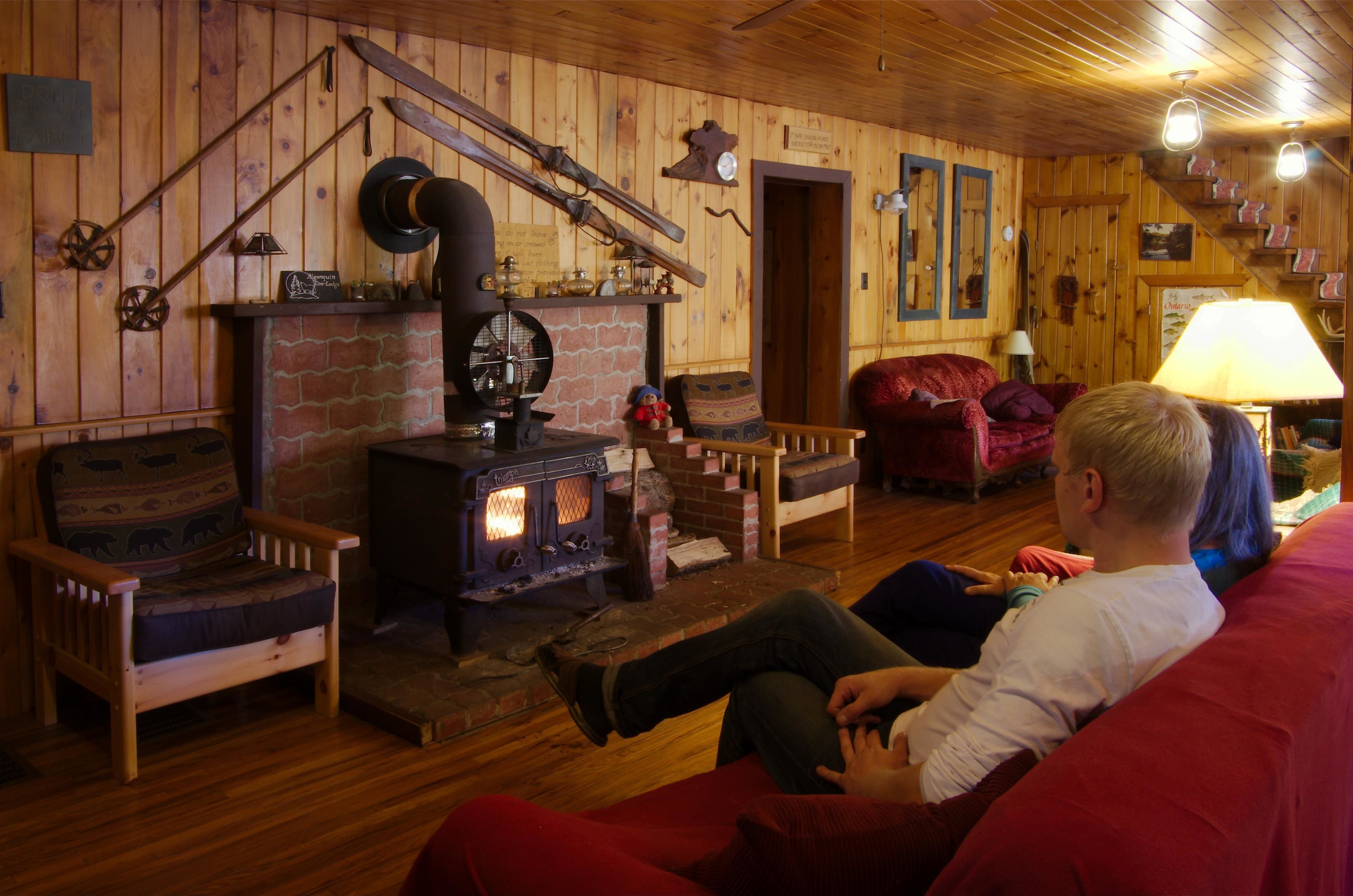 A cozy cabin interior with a wood-burning stove, rustic furniture, and a staircase leading to an upper level.