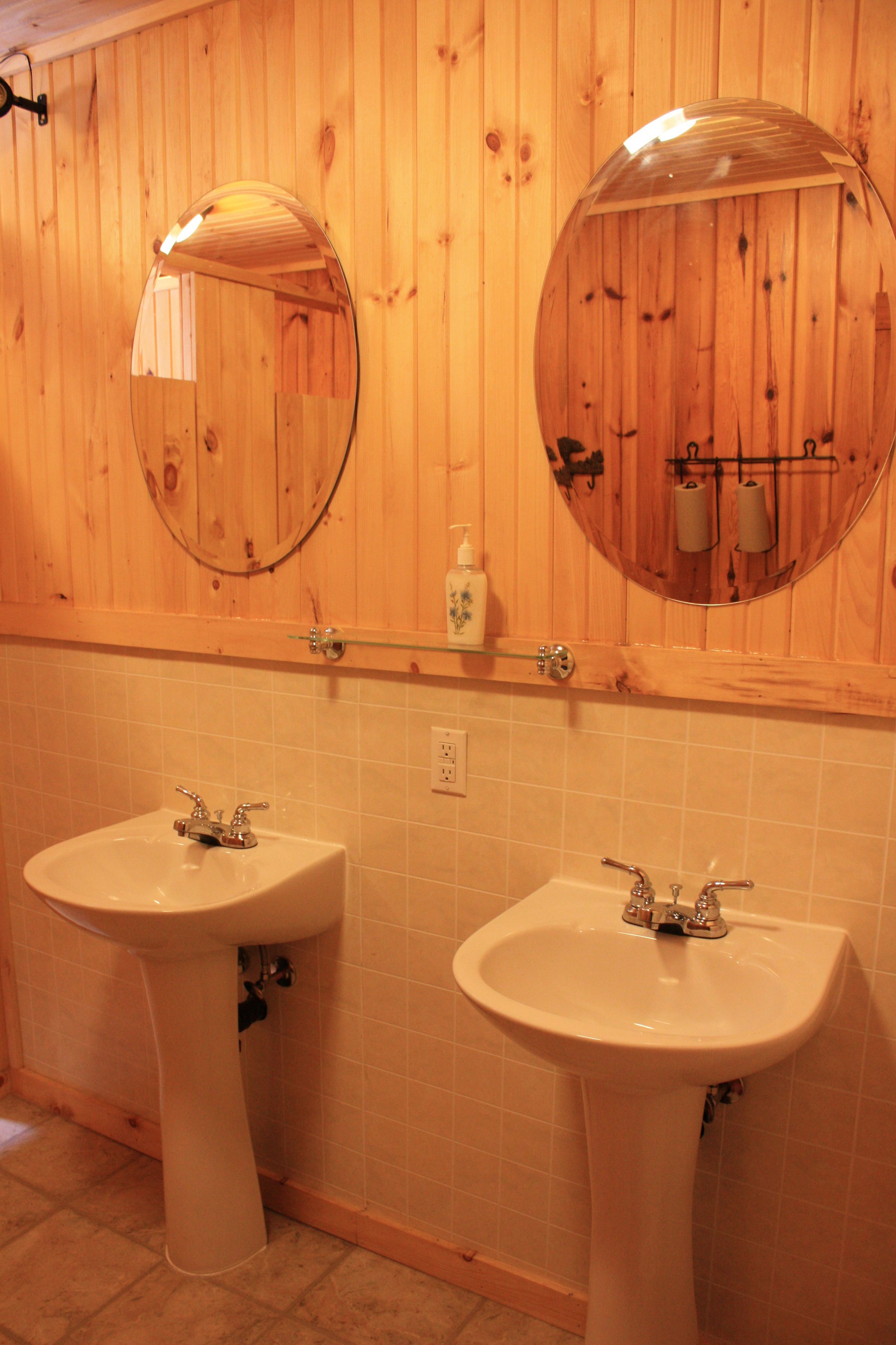 Un baño con paneles de madera, dos lavamanos y espejos redondos.