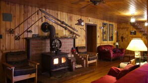 Una habitación acogedora con estufa de leña, un sofá rojo y una silla de madera.