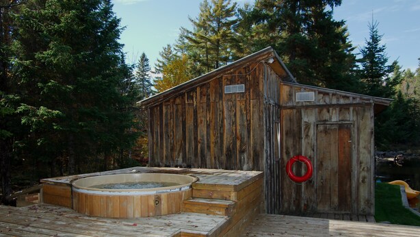 Una cabaña de madera con un jacuzzi y un flotador, rodeada de árboles.