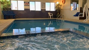 Une piscine intérieure avec un panneau indiquant la présence d’un sauveteur, une affiche présentant le règlement de la piscine et une chaise placée près du bord.