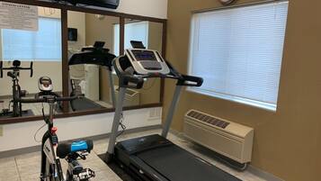 Un gimnasio con cinta de correr, bicicleta estática y un espejo.