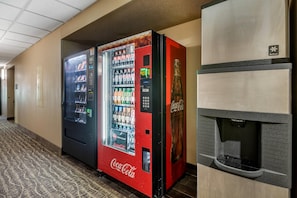 Un pasillo de hotel con una máquina expendedora de Coca-Cola y un dispensador de agua.