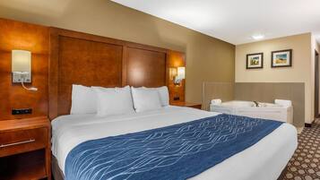 A hotel room with a large bed, a bedside table, a desk, a chair, a bathtub, and two framed pictures on the wall.