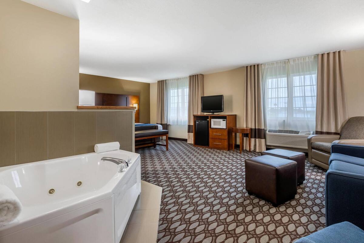 A hotel room with a large bathtub, a sofa, a desk with a television, and a window with curtains.