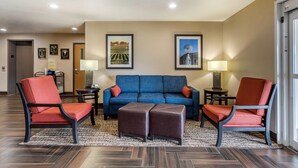 A hotel lobby with a blue sofa, red chairs, a coffee table, two lamps, framed pictures on the wall, and a patterned rug. - Comfort Inn Story City (Story City)
