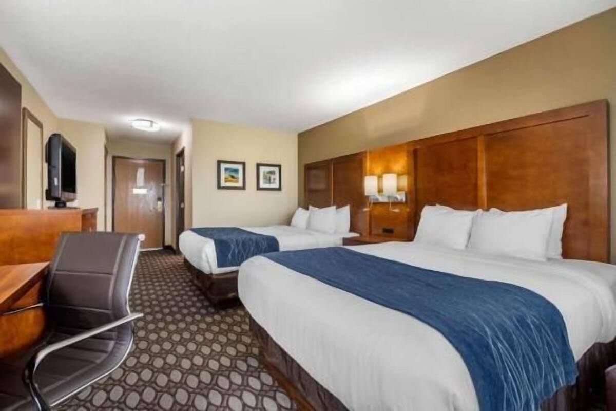 A hotel room with two beds, a desk, a chair, and a television.