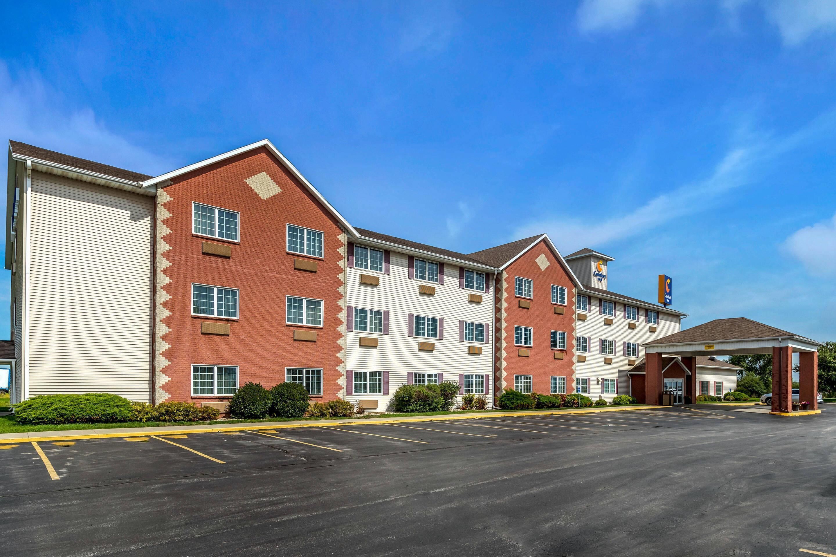 A multi-story hotel with a parking lot, a covered entrance, and a clear blue sky.