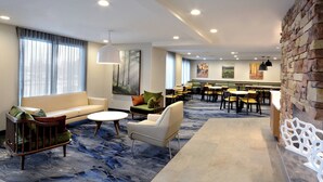 Un hall de hotel con diversas zonas de estar, incluyendo sofás y sillones, un área de comedor con mesas y sillas, y una pared decorativa de piedra.