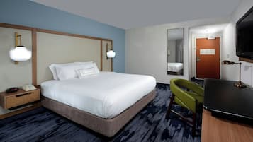 Quarto de hotel com cama, mesa de cabeceira, abajur, cadeira, escrivaninha, televisão e espelho.
