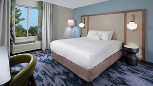 Una habitación de hotel con una cama grande, dos lámparas de noche, una silla y un ventanal con cortinas.