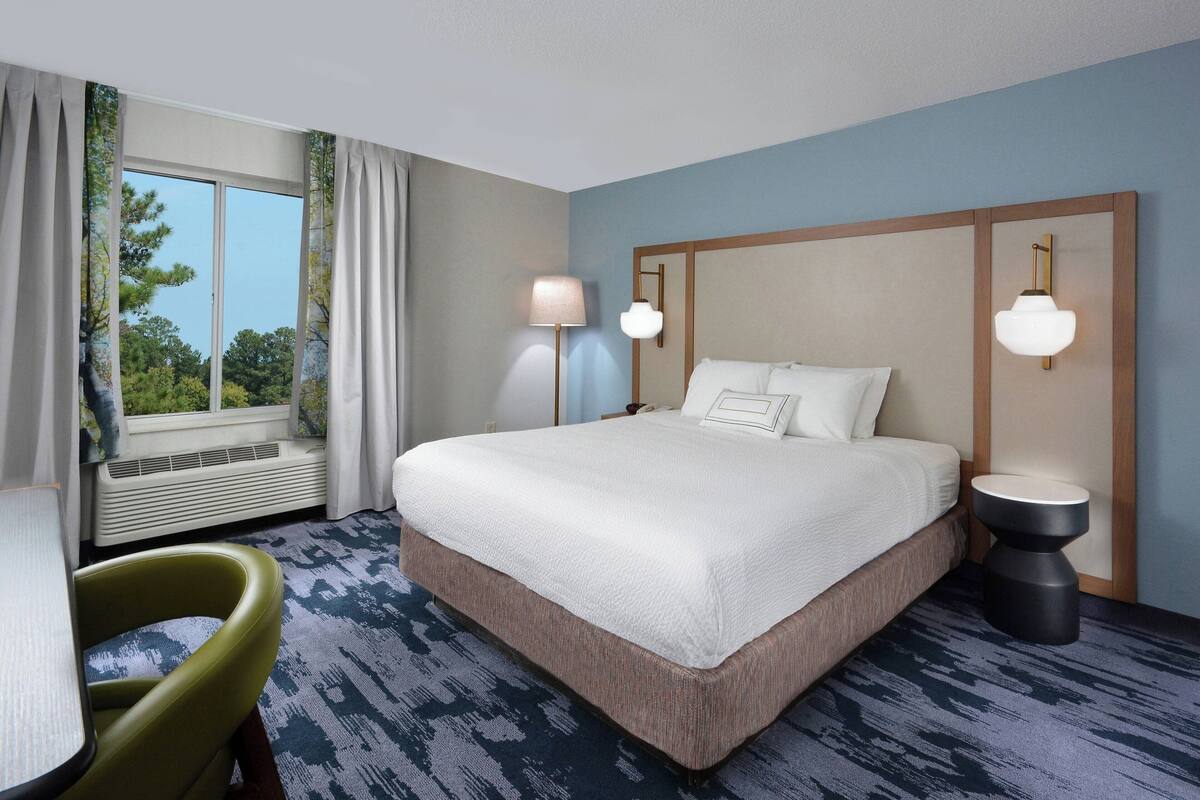A hotel room with a large bed, two bedside lamps, a chair, and a window with curtains.