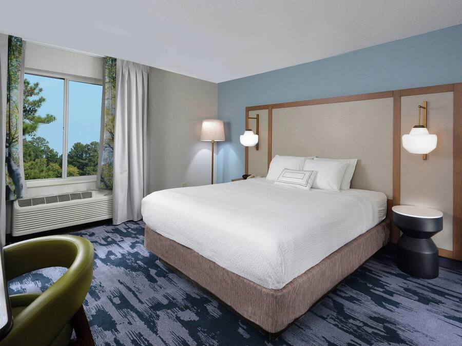 A hotel room with a large bed, two bedside lamps, a chair, and a window with curtains.