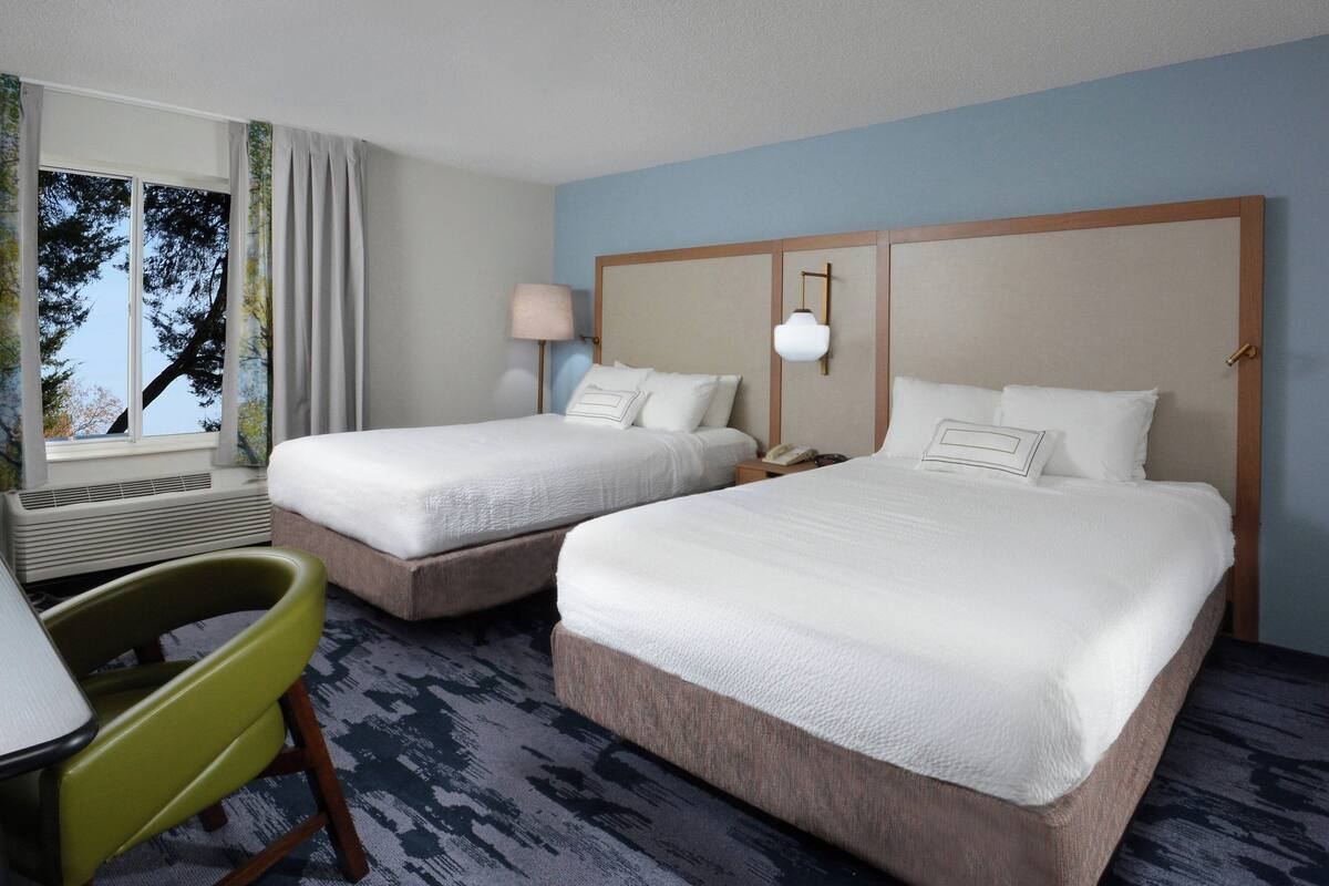 A hotel room with two beds, a desk, and a chair.