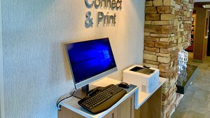 Un mostrador de recepción con monitor de computadora, teclado e impresora. En la pared detrás del mostrador hay un letrero que dice 'Connect & Print'.