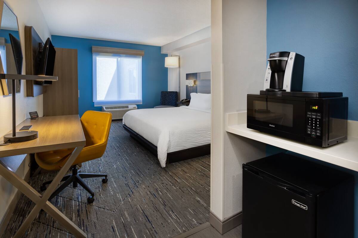 Ein Hotelzimmer mit Bett, Schreibtisch mit Stuhl, einer Mikrowelle und einem Kühlschrank.
