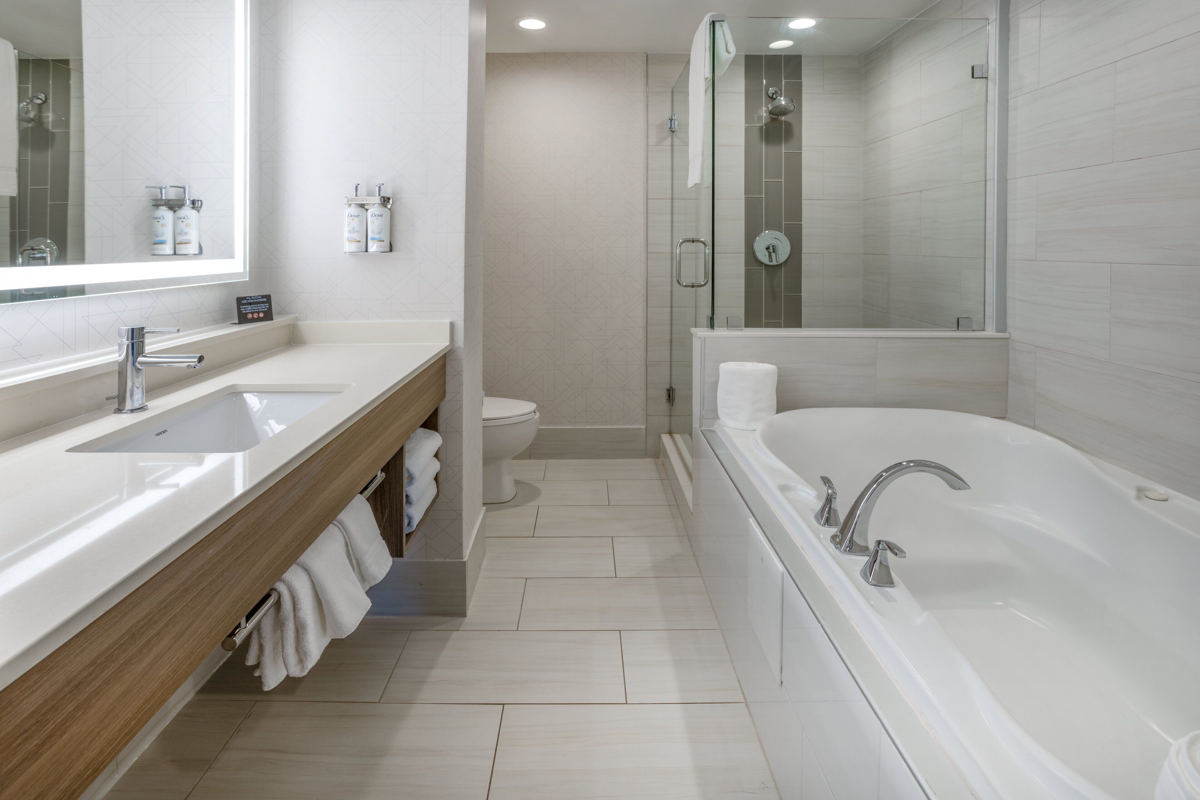 A modern bathroom with a large bathtub, two sinks, a toilet, and a glass-enclosed shower area.