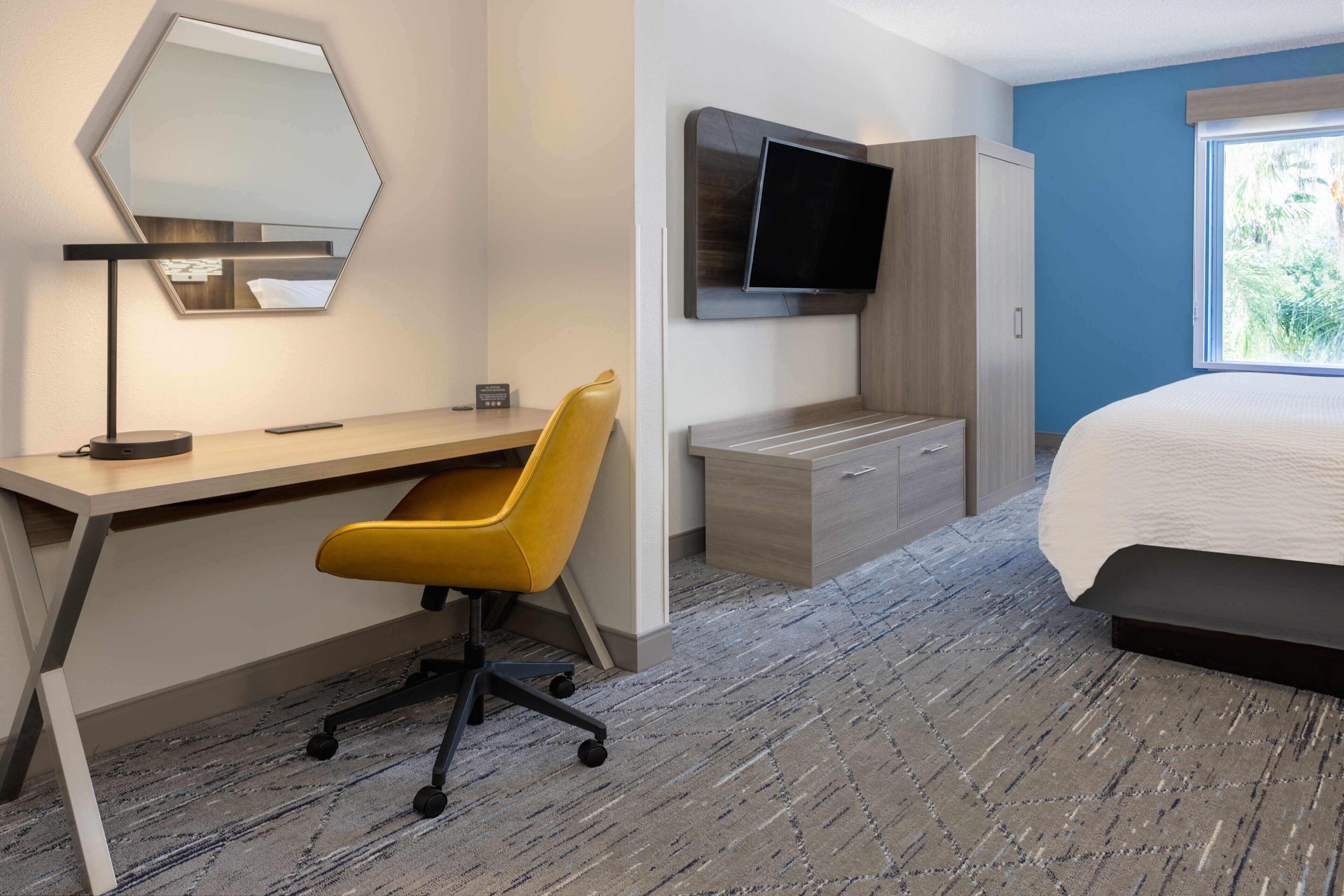 A hotel room with a desk, chair, TV, wardrobe, and a bed.