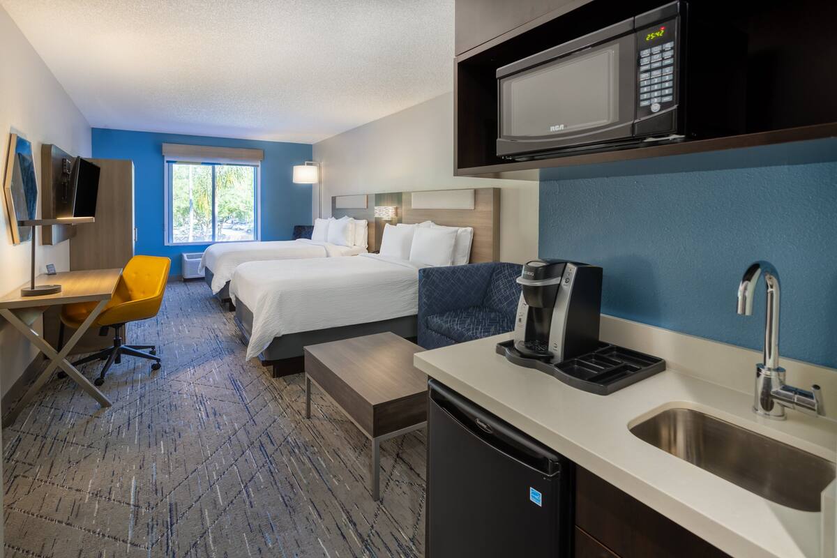 Ein Hotelzimmer mit einem Bett, einem Schreibtisch mit Stuhl, einer Mikrowelle, einer Kaffeemaschine und einem Waschbecken.