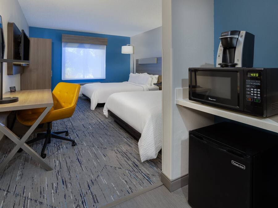 Habitación de hotel con dos camas, un escritorio con silla, un microondas y un refrigerador.