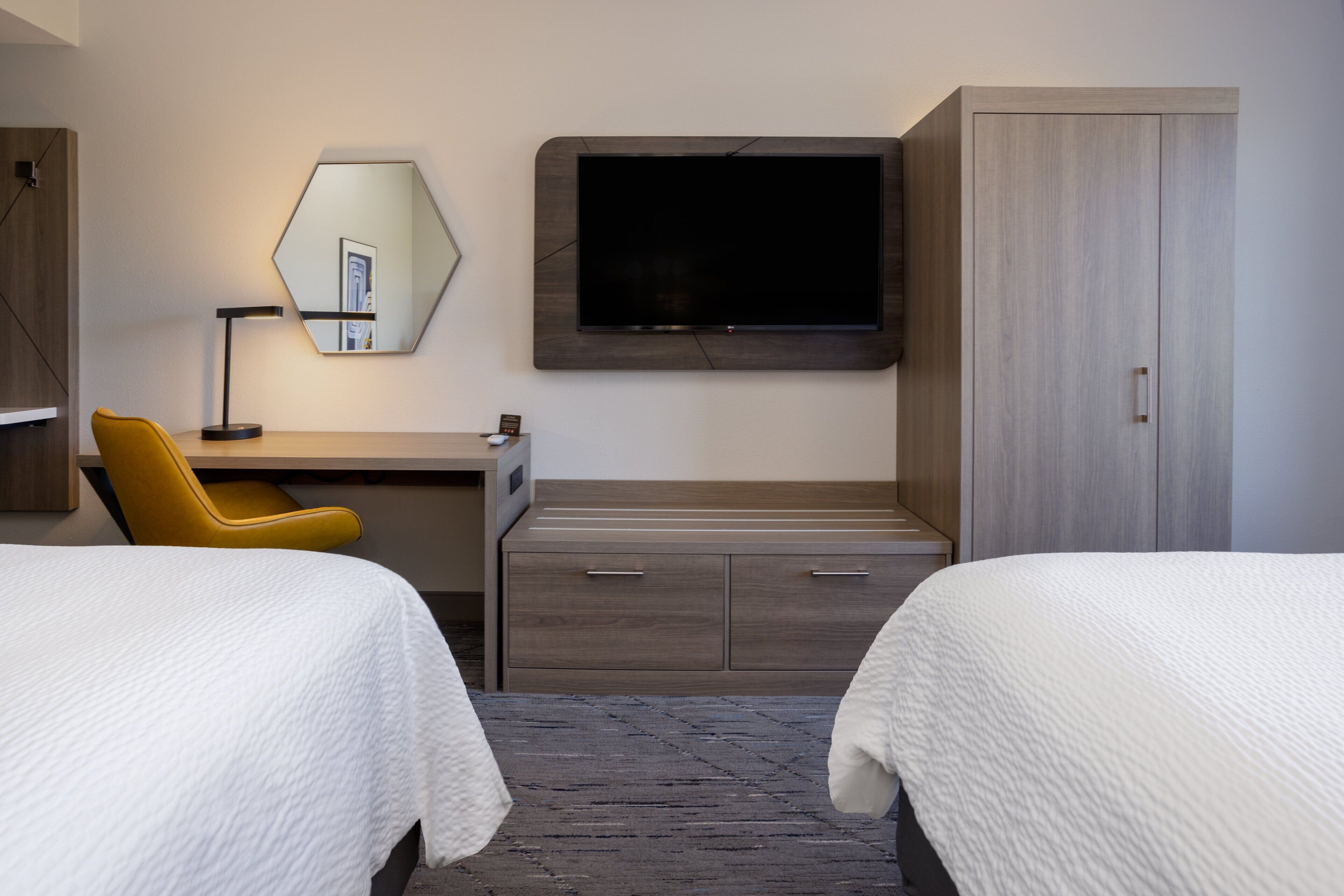 A hotel room with two beds, a desk, a chair, a television, and a wardrobe.