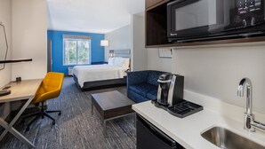 A hotel room with a bed, a desk, a chair, a microwave, a coffee maker, and a sink.