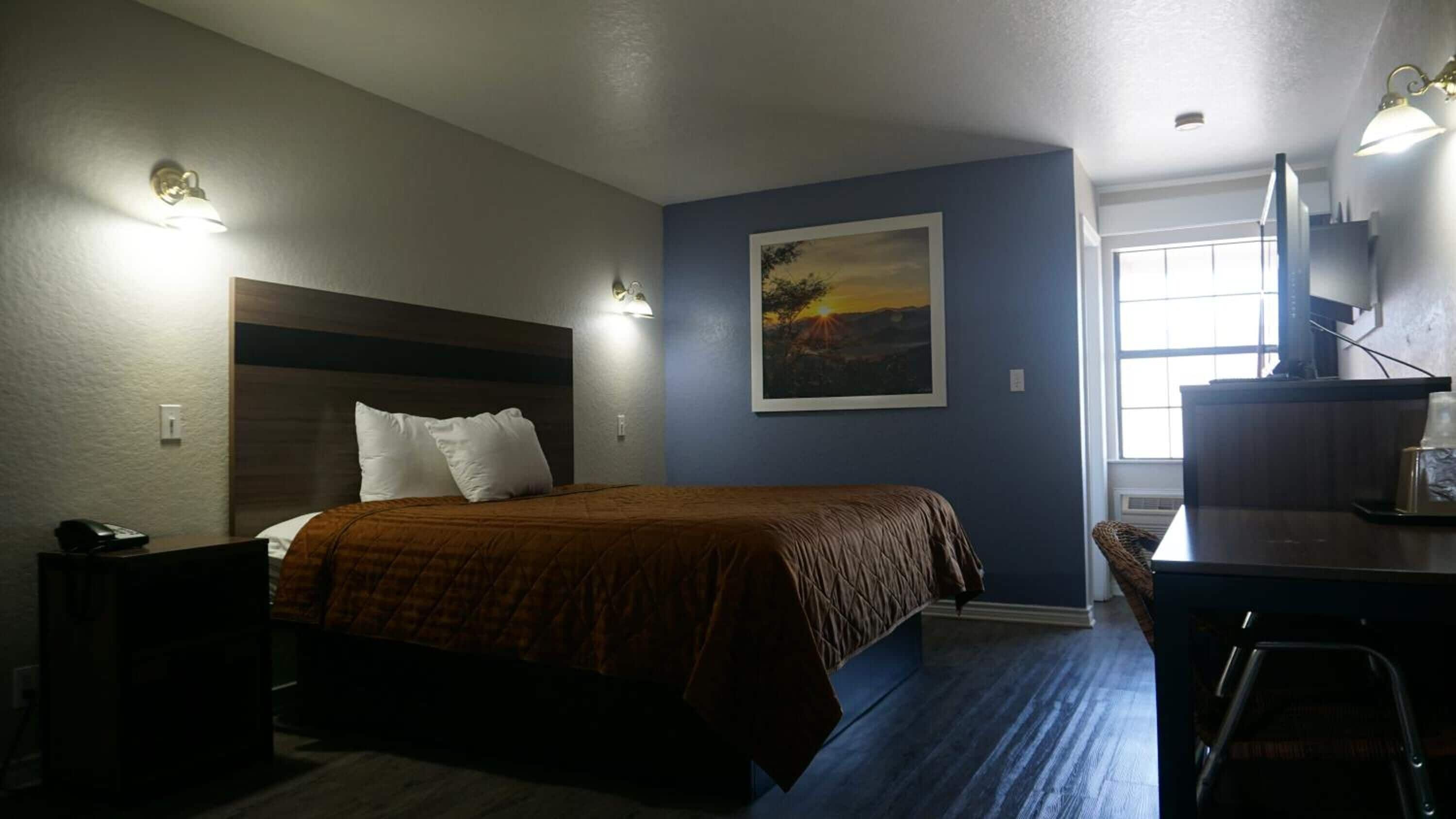 Ein Hotelzimmer mit Bett, Schreibtisch, Stuhl, einem Bild an der Wand und einem Fenster.