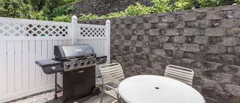 An outdoor patio with a grill, a round table, and chairs.