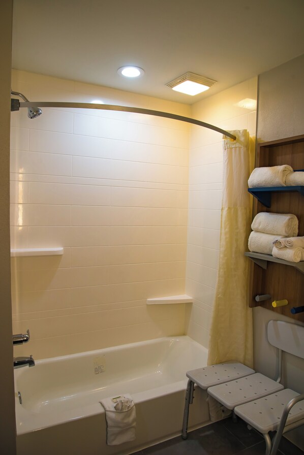 A bathroom with a bathtub, a shower curtain, a shelf with towels, and a step stool.