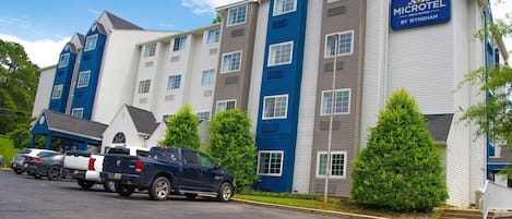 A Microtel Inn & Suites building with a parking lot, a blue pickup truck, and green trees.