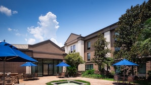 Un patio con mobiliario exterior, una fuente y un edificio con varias ventanas y techo plano.