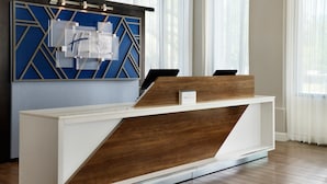 Un mostrador de recepción con diseño moderno, que presenta un patrón geométrico en la pared de fondo y una combinación de acabados en blanco y madera en el mostrador.