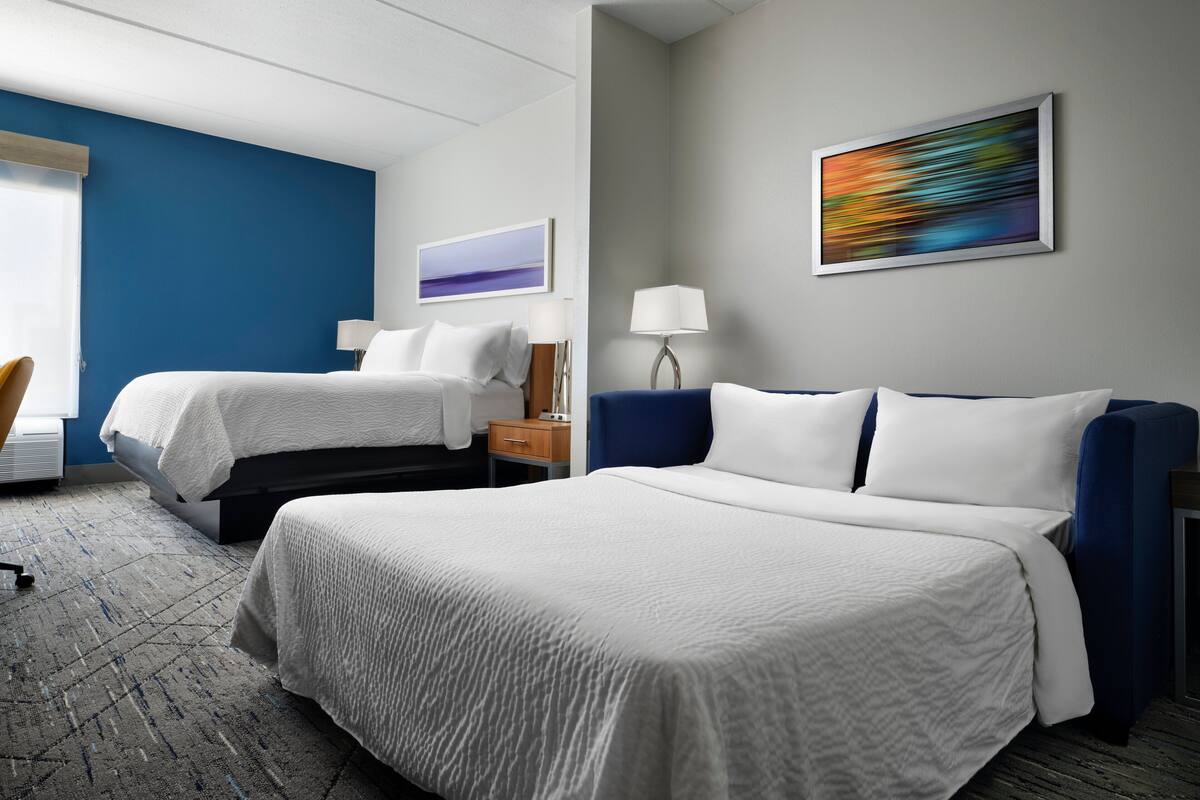 Habitación de hotel con dos camas, un escritorio, una silla y un cuadro en la pared.