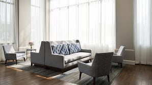 Una sala moderna con un sofá gris, dos sillones y una mesa de centro. Ventanas amplias con cortinas translúcidas permiten que la luz natural ilumine el espacio.