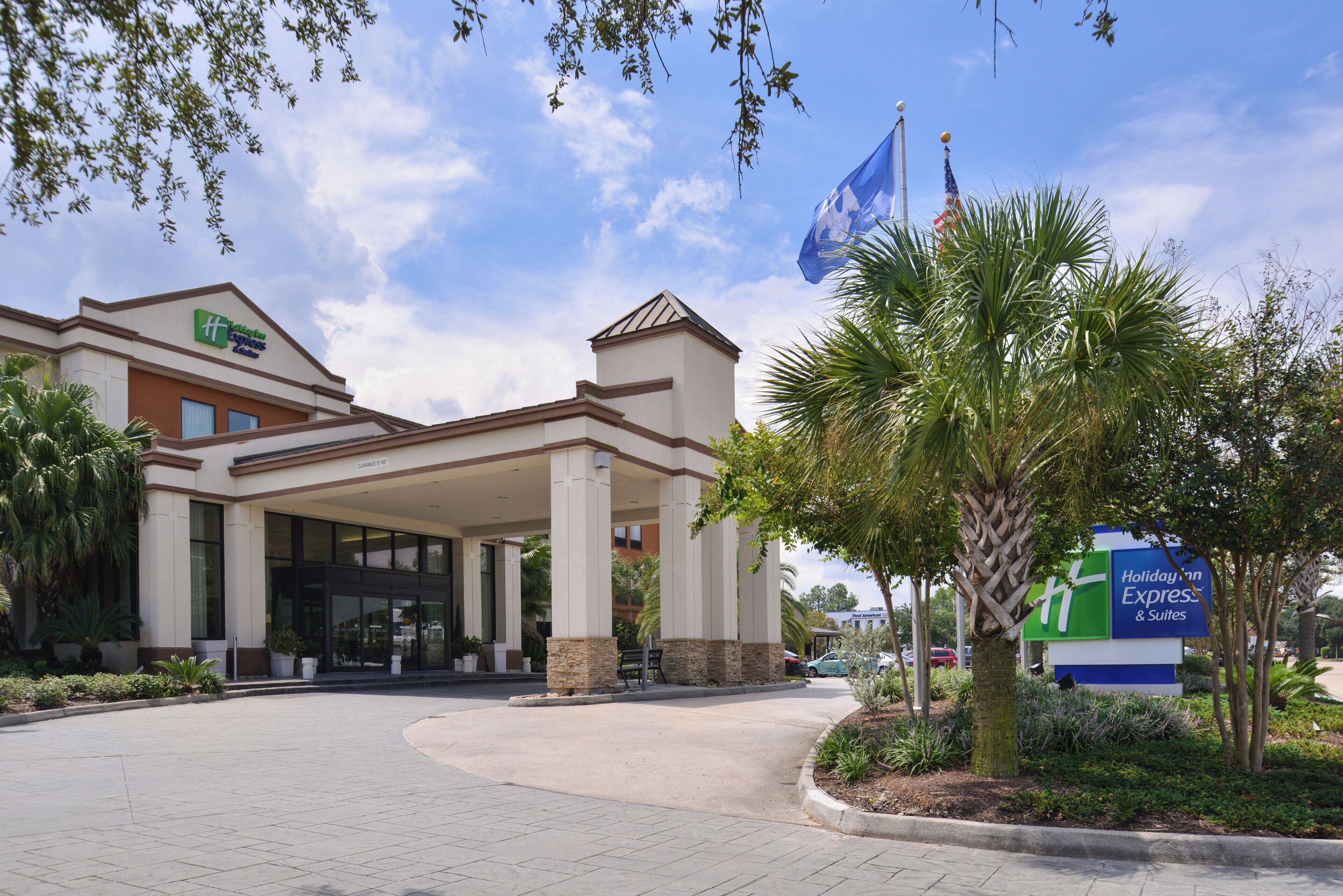 A Holiday Inn Express & Suites building with a covered entrance, palm trees, and a clear sky.