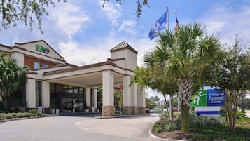 A Holiday Inn Express & Suites building with a covered entrance, palm trees, and a clear sky.