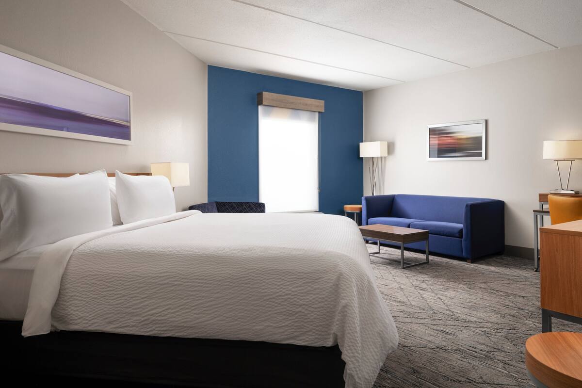Una habitación de hotel con una cama grande, un sofá azul, una mesita y una lámpara.