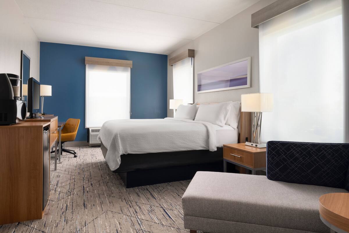 Una habitación de hotel con cama, escritorio con computadora, una silla, un sofá y una lámpara.