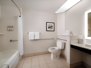 A modern bathroom with a bathtub, toilet, and sink. There are two towels hanging on a rack, a framed picture on the wall, and a shower curtain.