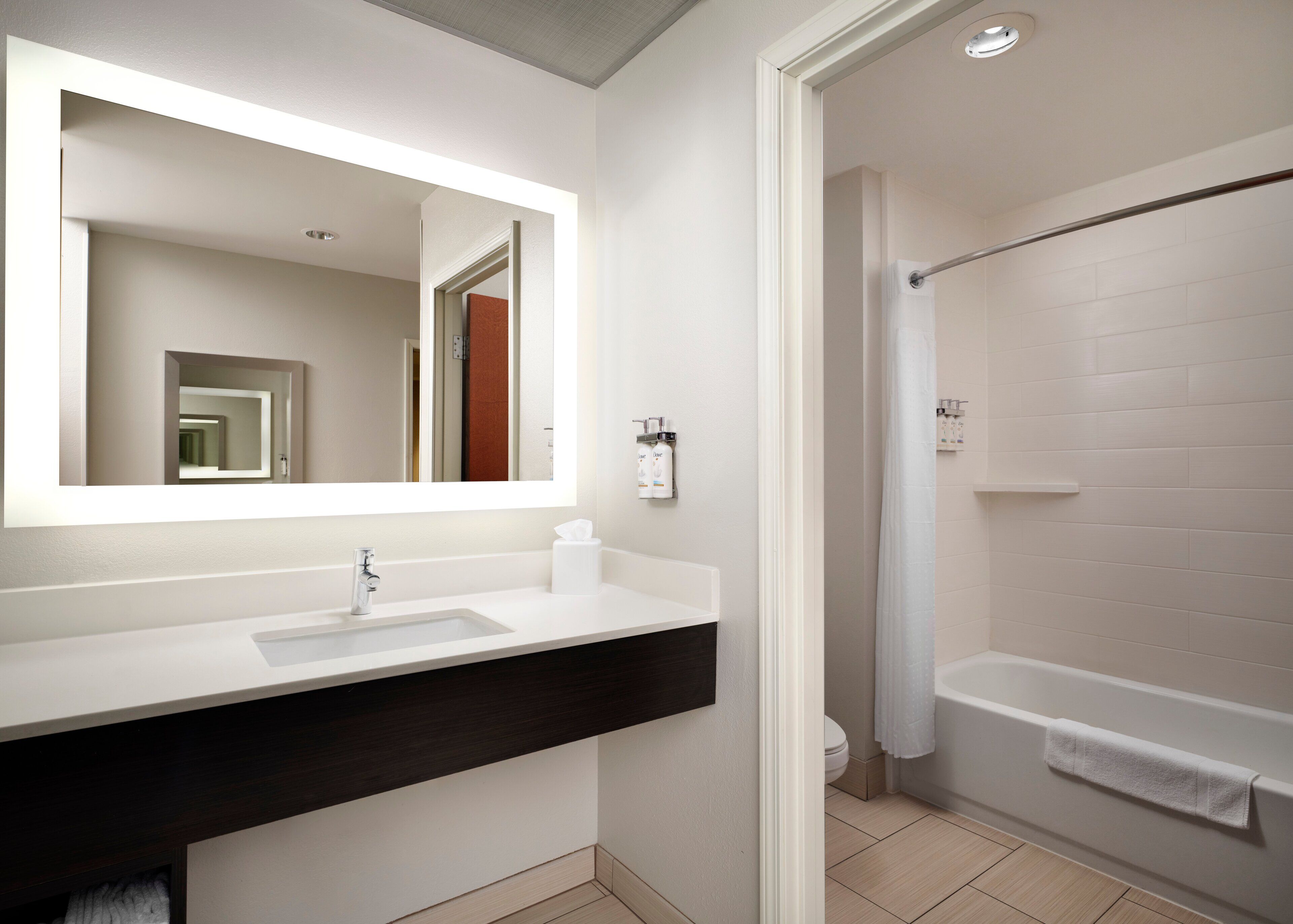 A modern bathroom with a white sink, dark countertop, and a large mirror.