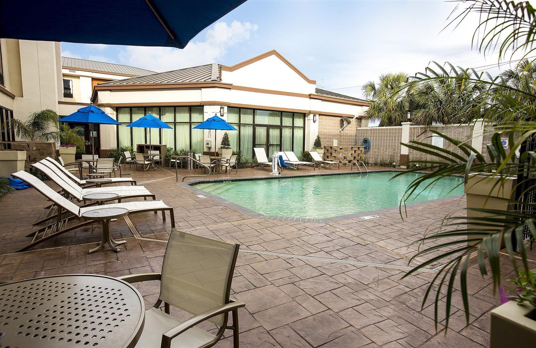 Zona de piscina con sillones, sombrillas y un edificio al fondo.