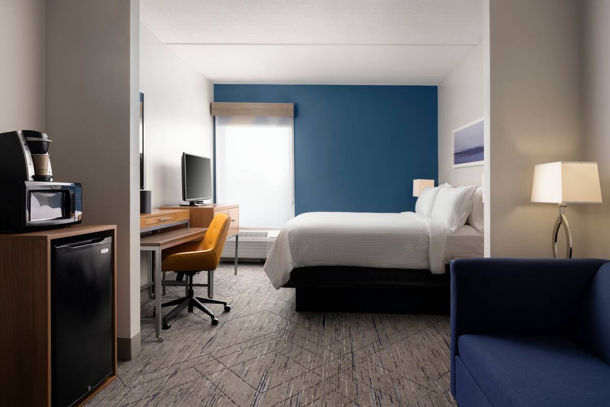 Una habitación de hotel con cama, escritorio, silla, televisión, cafetera y lámpara.