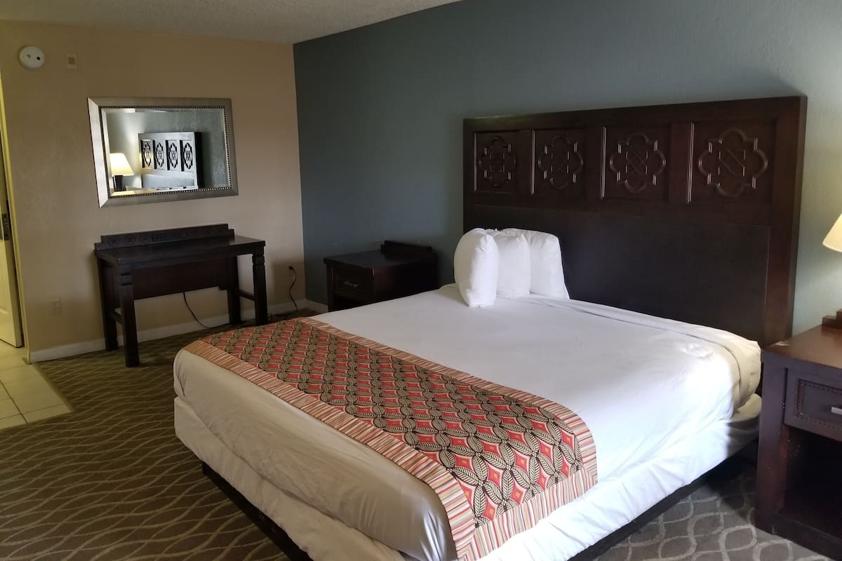 A hotel room with a large bed, a wooden headboard, a desk, and a mirror.