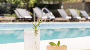 A poolside setting with two drinks on a tray, a pool, and lounge chairs in the background.