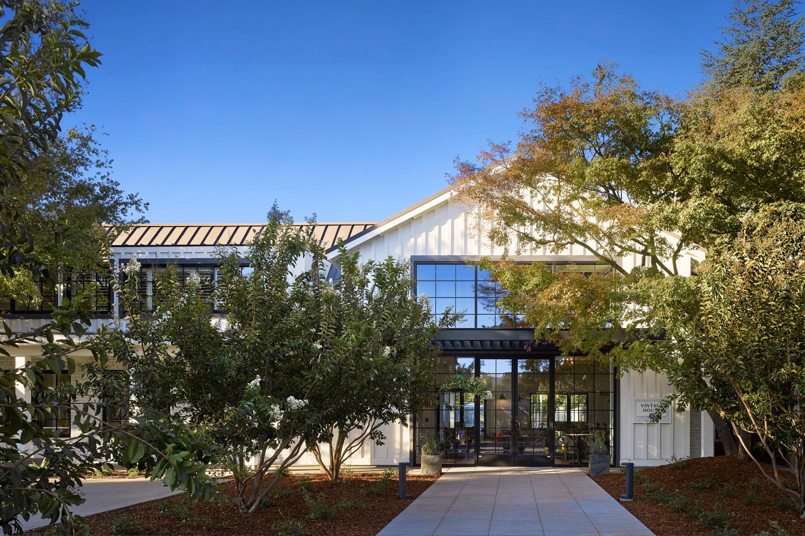 A modern building with a glass facade, a covered entrance, and a well-maintained garden area.