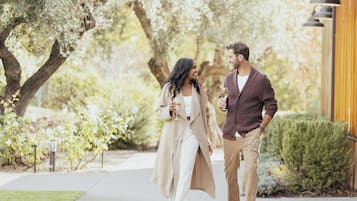 A couple walking on a sidewalk with trees and a building in the background.