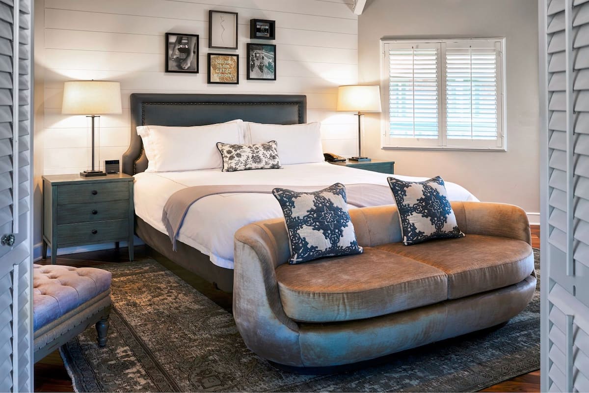 A bedroom with a bed, two nightstands, a bench, and a window with blinds.