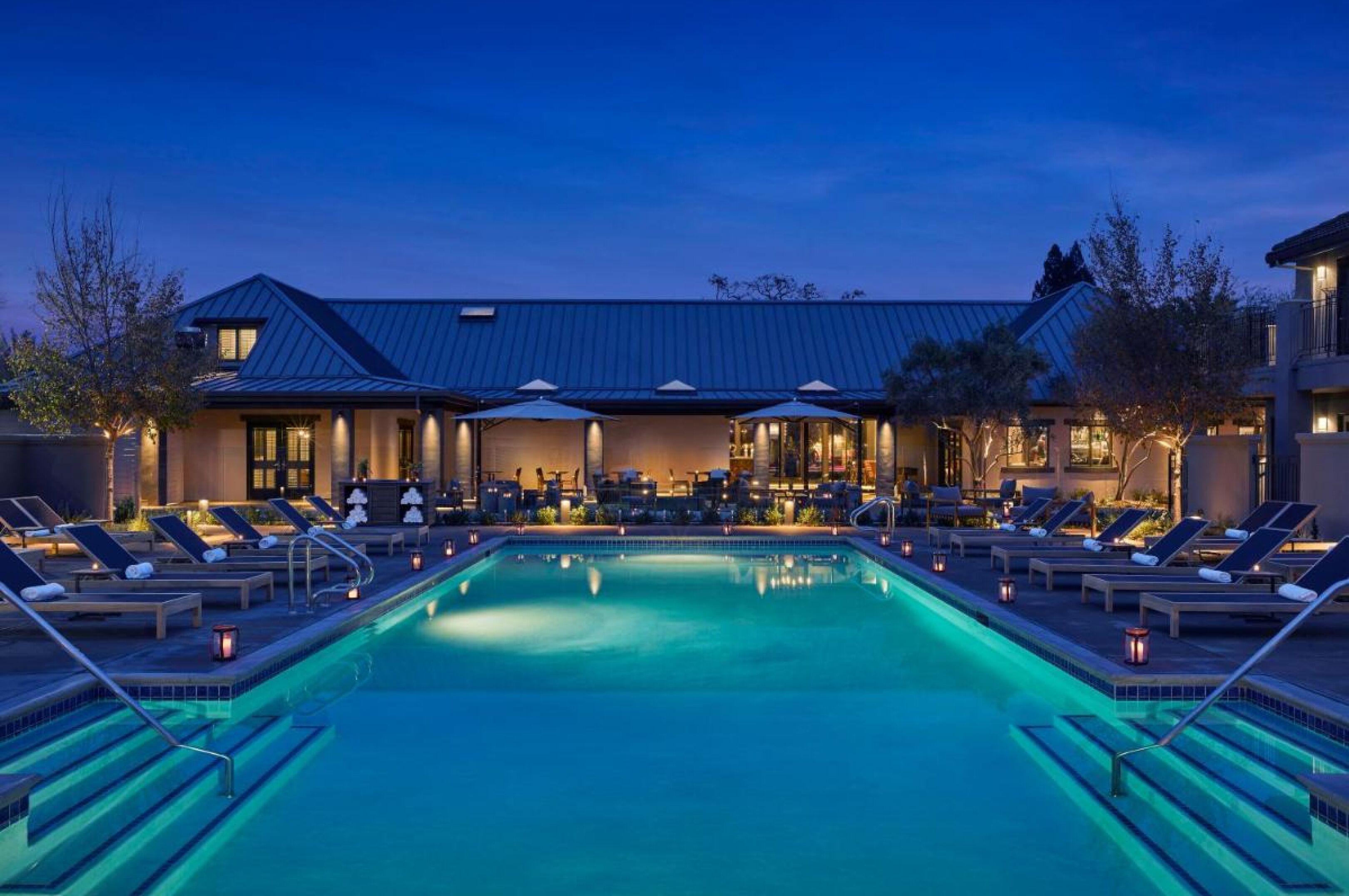 A poolside area with lounge chairs and a swimming pool, surrounded by a building with a metal roof.