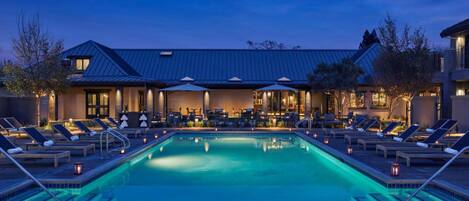 A poolside area with lounge chairs and a swimming pool, surrounded by a building with a metal roof.